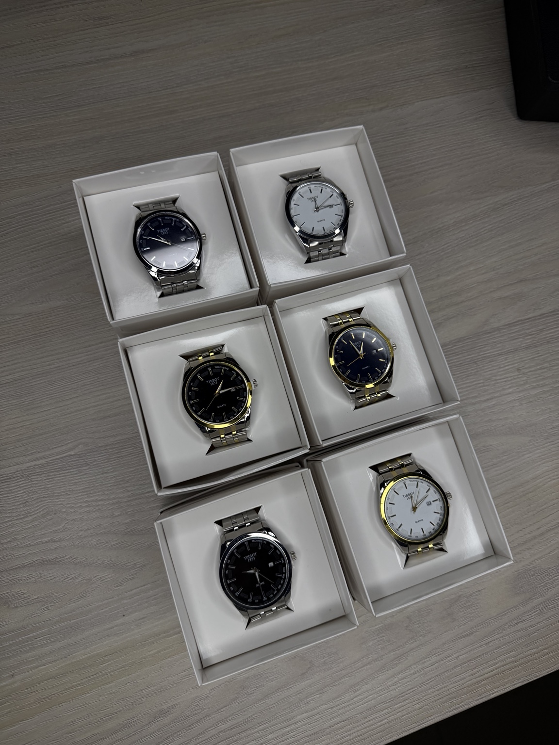 Seis relojes de acero con esferas claras y oscuras, cada uno en su caja blanca individual.