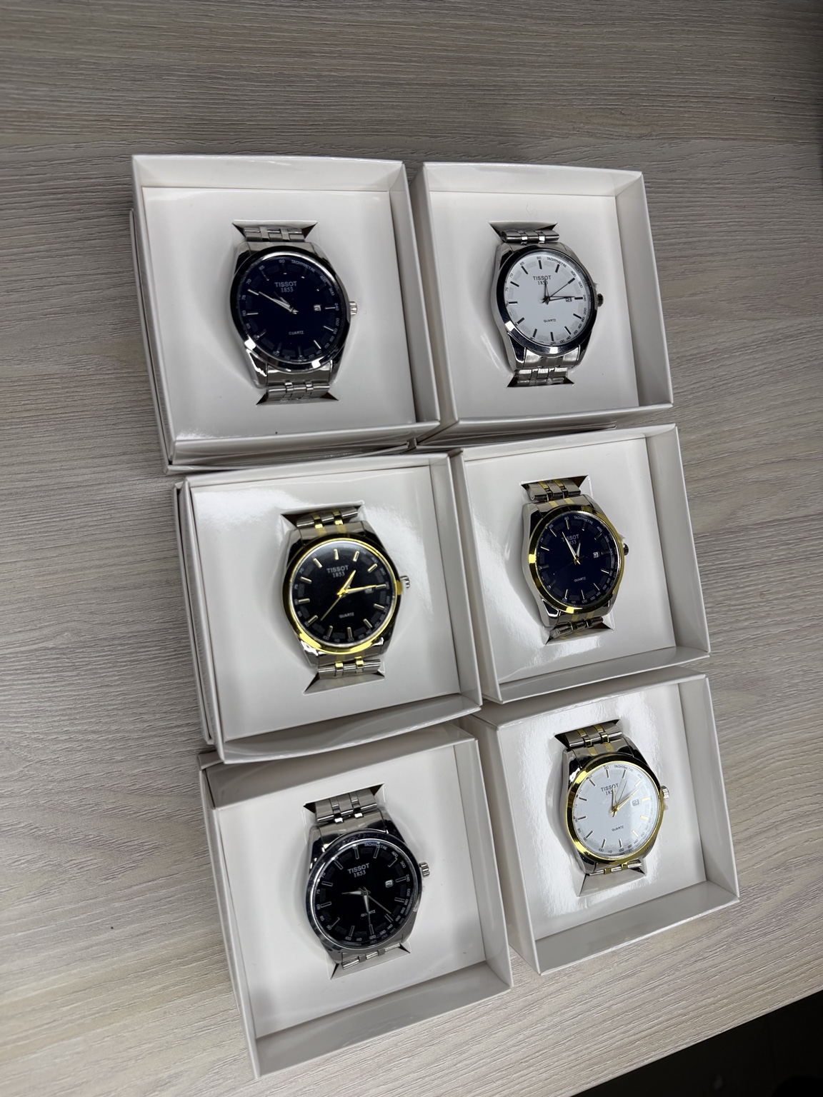 Seis relojes de acero y acero dorado ordenados en sus cajas blancas individuales.