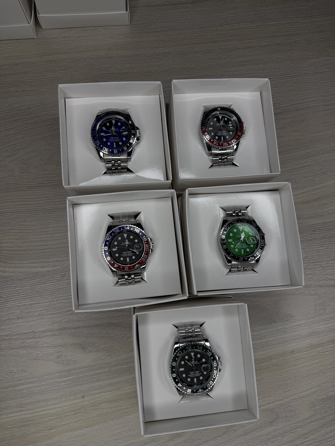 Cinco relojes de acero, cada uno presentado dentro de su caja blanca individual.